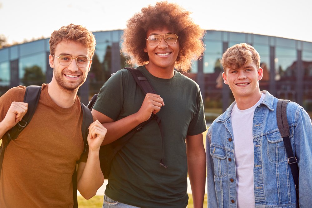 portrait of three male university or college student standing outdoors by modern campus building